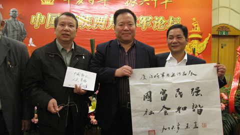 A16、王直老将军为第二届“中国海峡两岸将军书画展”题字：“国富民强， 社会和谐”。李大维将军为《华夏名人一千家》宣纸封题字：“中国强大，人民幸福”。左起：王银茂、李大维、黄仁福